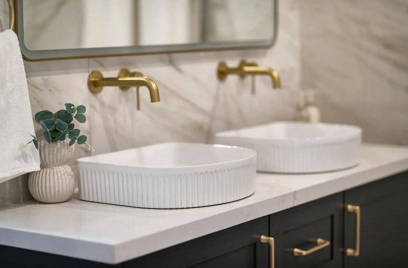 Twin fluted white basins with wall-mounted brushed brass tapware on a stone vanity