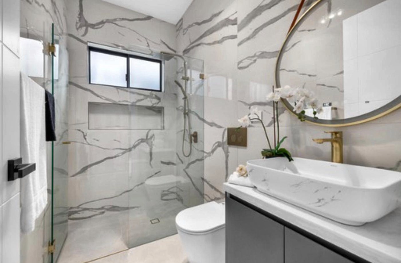 A marble-look ensuite with a frameless shower, a vessel basin and brushed brass tapware