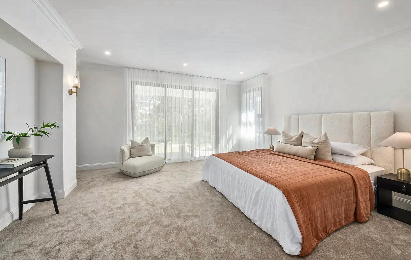 A calm master suite with a tall upholstered bedhead, sheer curtains and soft carpet