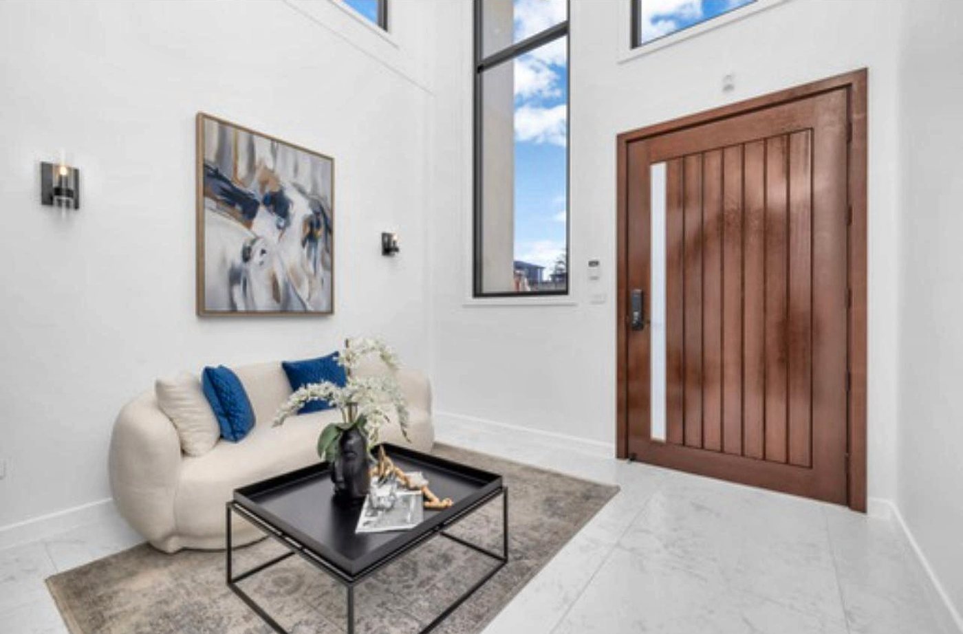 A double-height entry with a timber pivot front door and a curved cream sofa