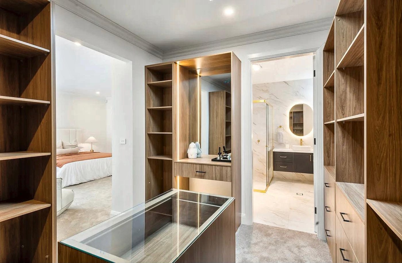 A walk-in robe with open oak shelving and a glass-topped island, leading to the ensuite